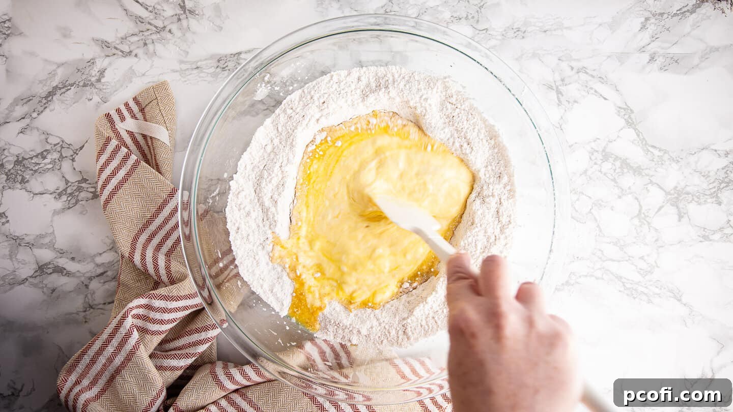 Folding dry ingredients into wet, showing the beginning stages of mixing cranberry orange muffin batter with a silicone spatula.