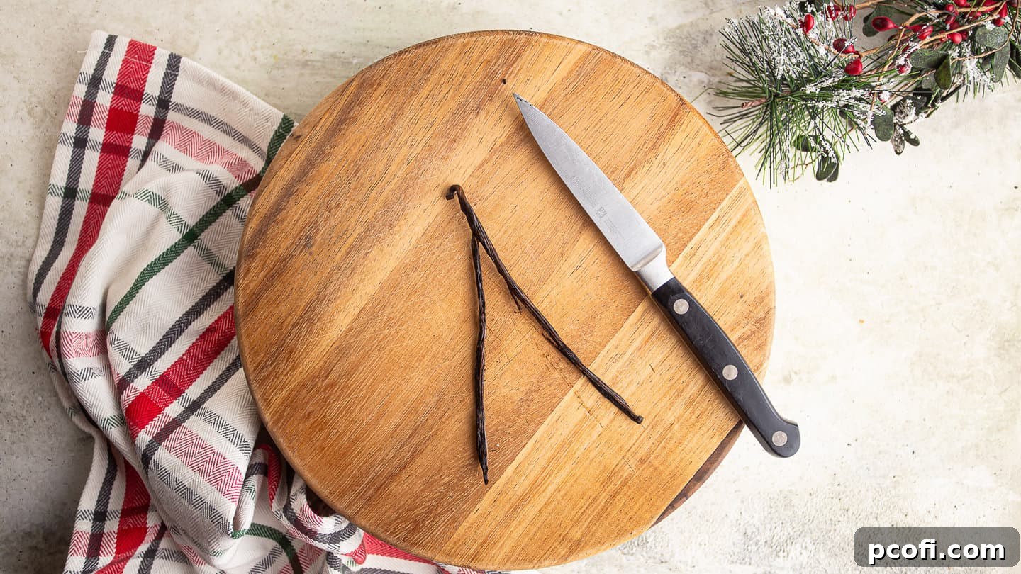 Carefully splitting a vanilla bean lengthwise with a sharp paring knife on a cutting board to expose the seeds inside for optimal flavor extraction.