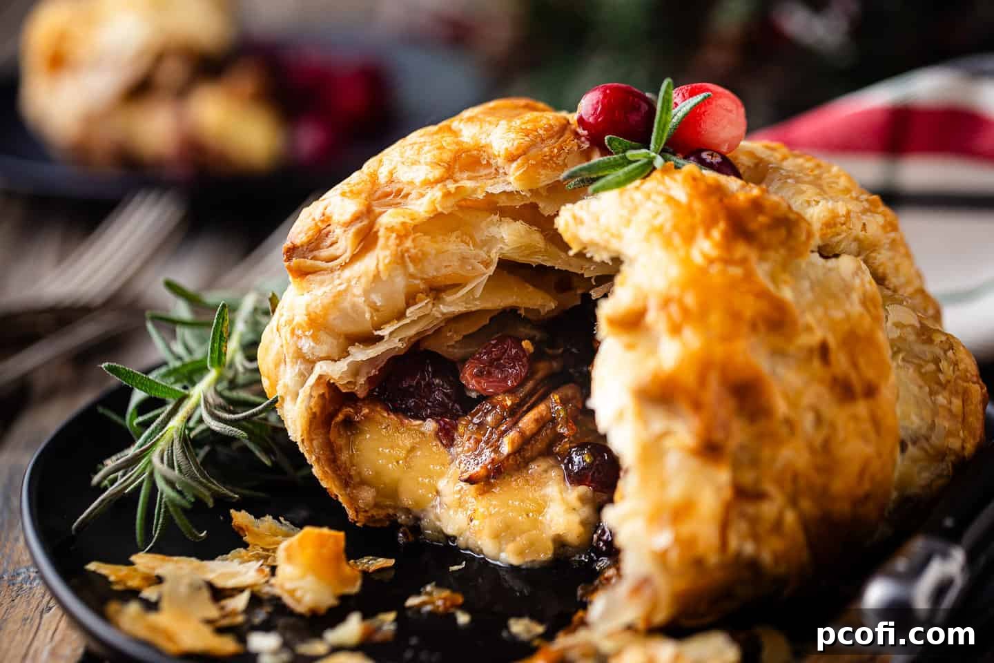 A beautifully baked brie puff pastry, adorned with wintry fruits, nuts, and fresh herbs, ready to be enjoyed.