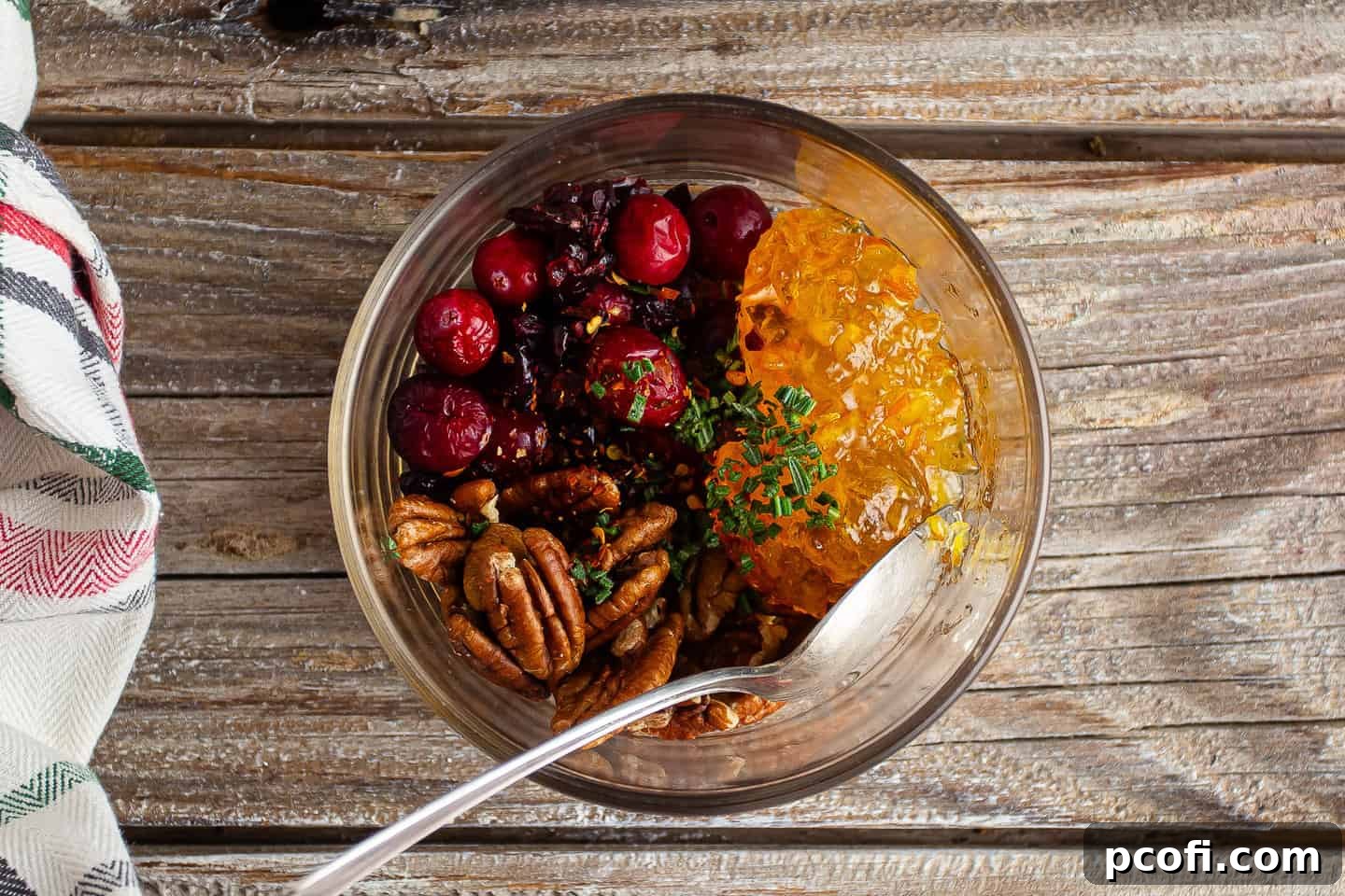 Cranberries, pecans, marmalade, rosemary, and crushed red pepper flakes, neatly arranged in a glass bowl before mixing.