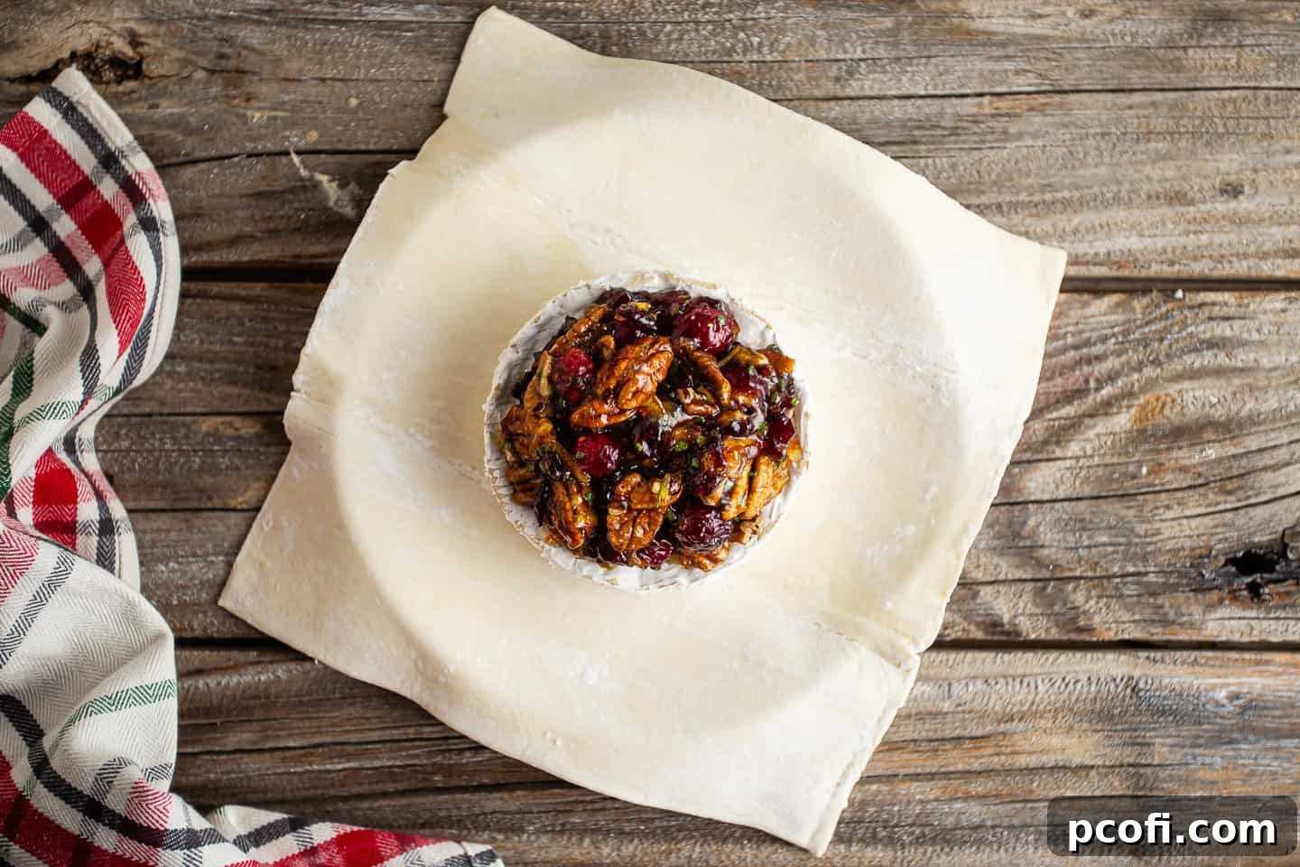 A wheel of brie cheese, centered on a puff pastry sheet, generously topped with the vibrant cranberry pecan jam mixture.