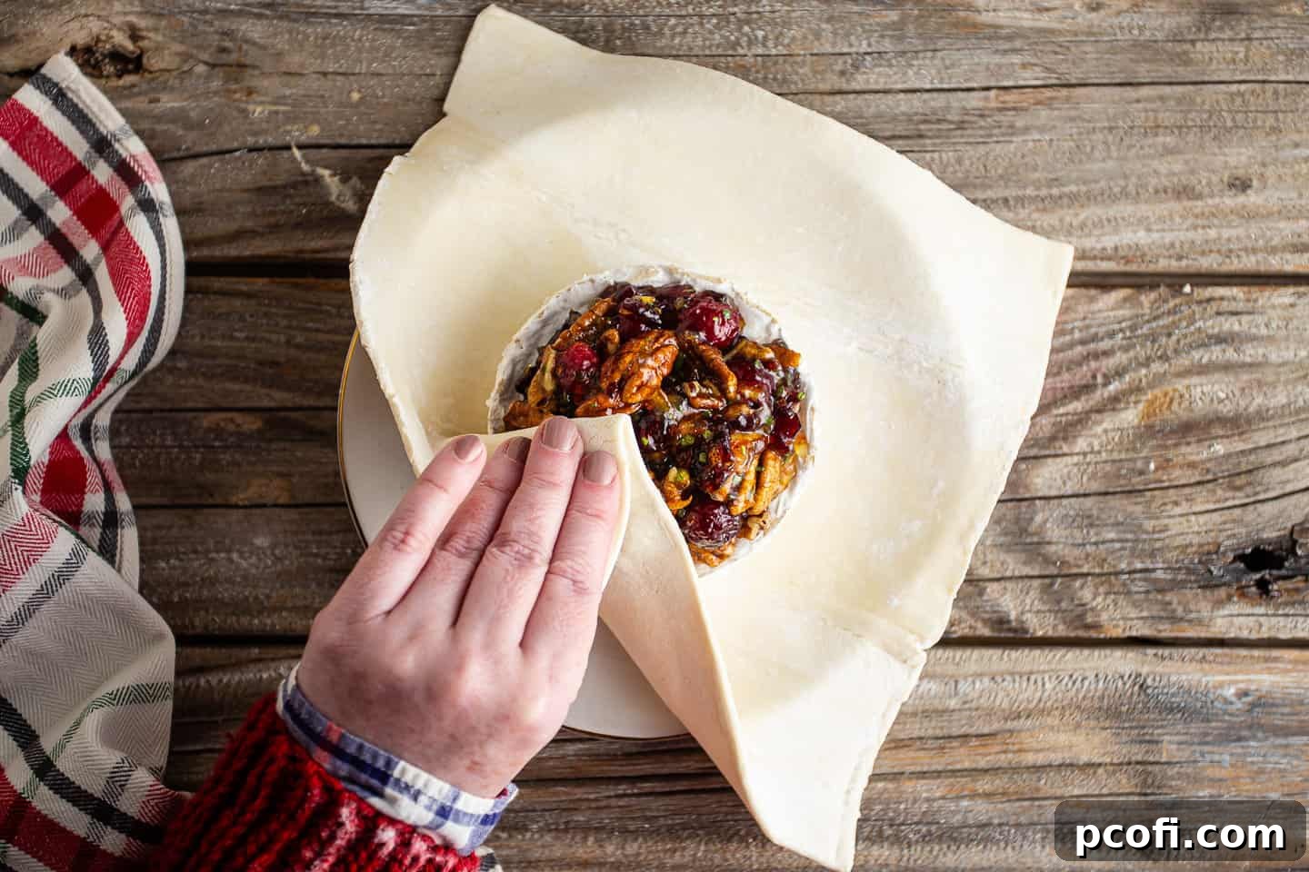 A partially wrapped brie and jam in puff pastry, showing the process of folding the pastry sides upwards to encase the filling.
