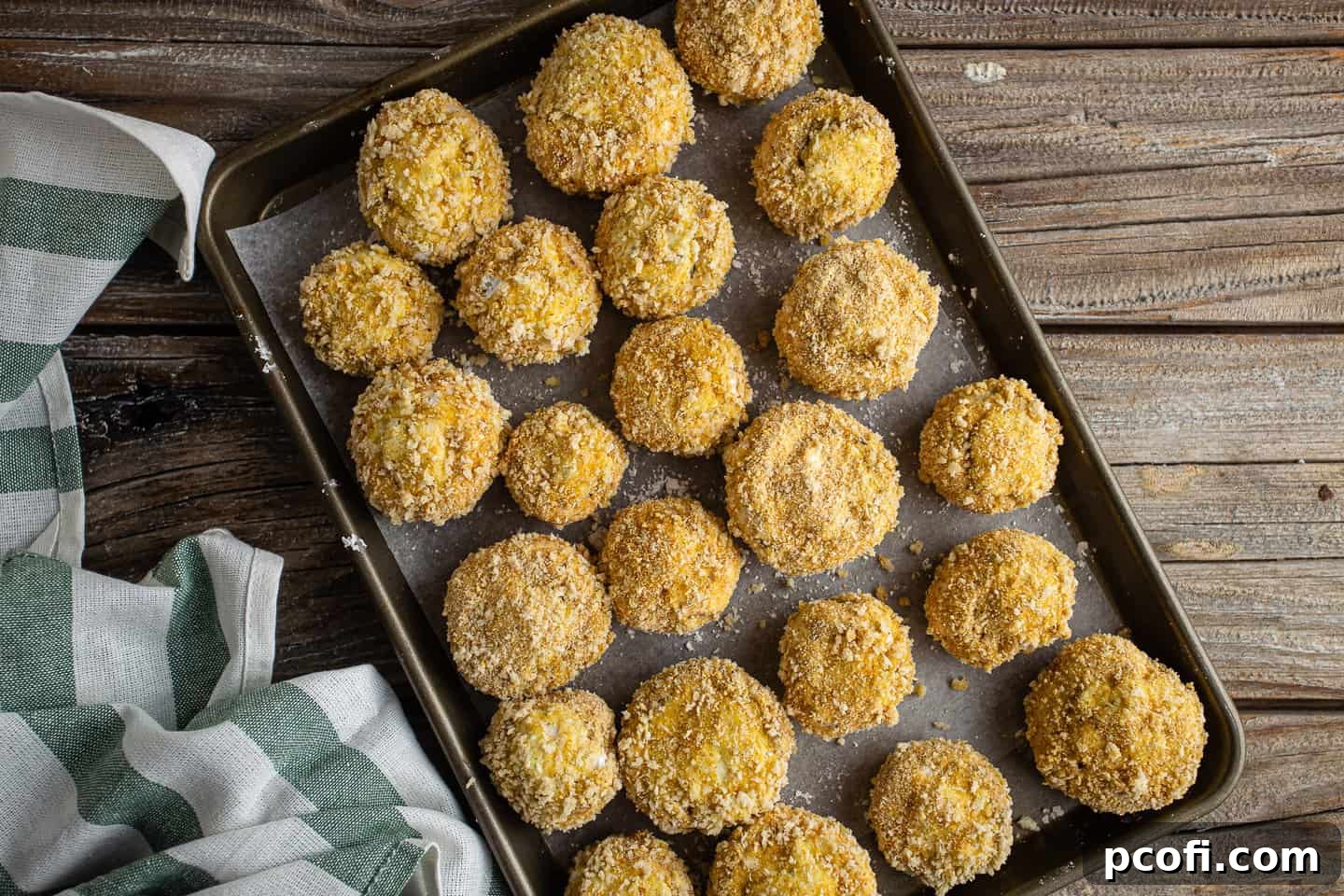 Breaded stuffed mushrooms on a parchment-lined baking sheet.