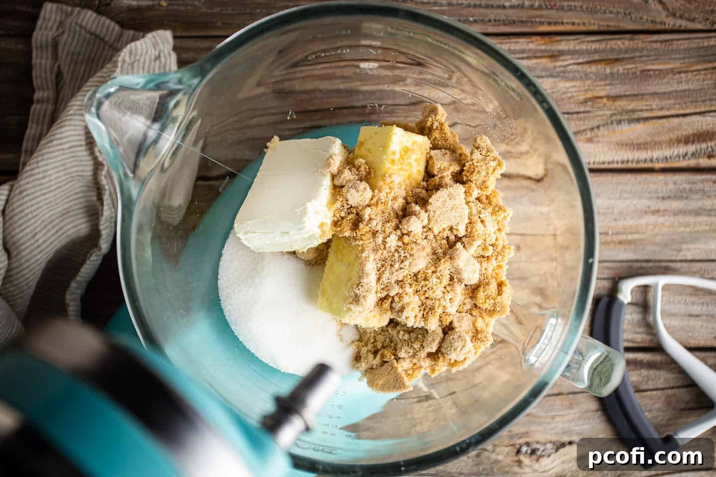 A visual depiction of butter, cream cheese, brown sugar, and white sugar combined in a large glass mixing bowl, ready for creaming.
