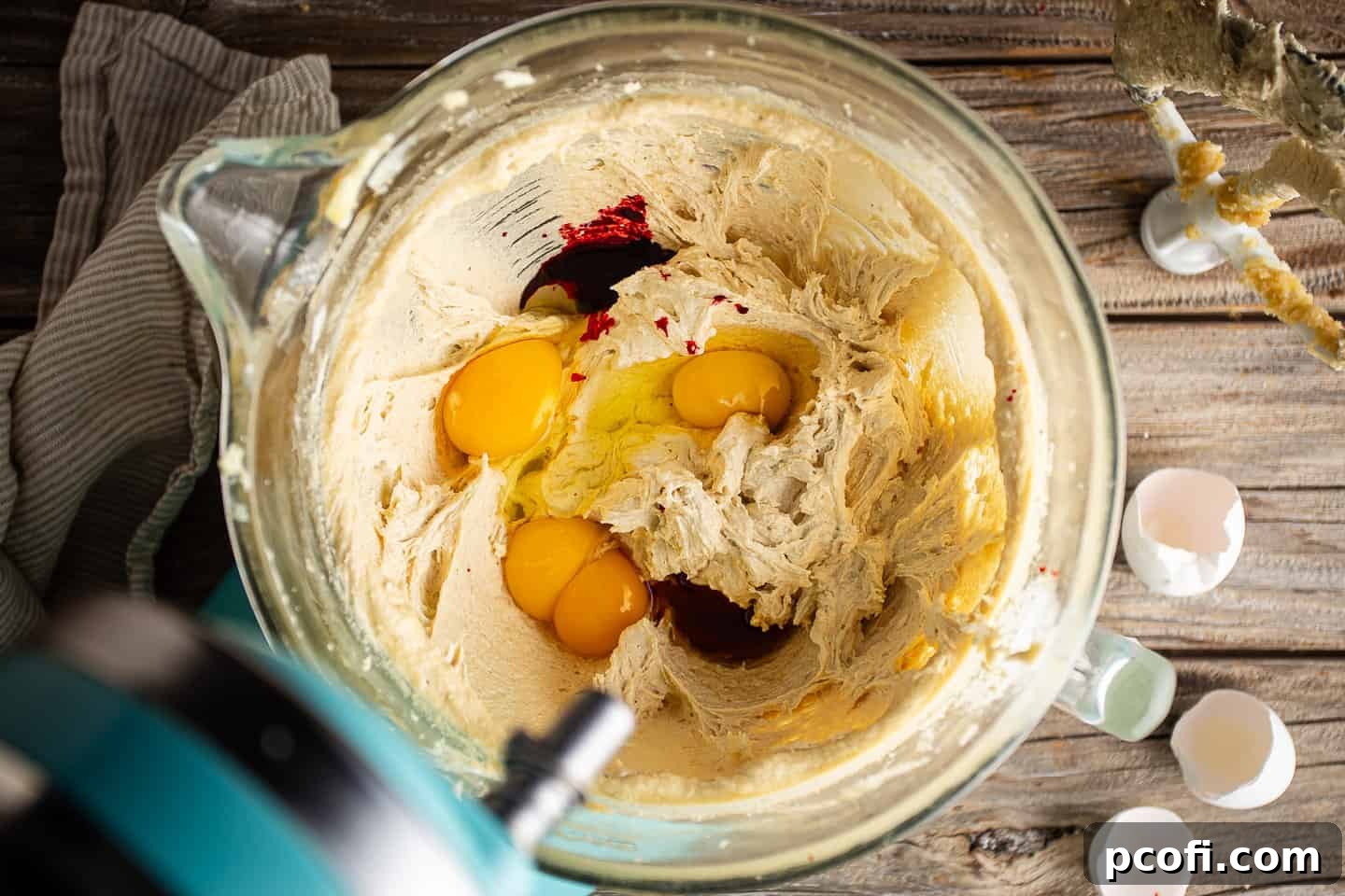 The process of adding eggs, vibrant red food coloring, and aromatic vanilla extract to the red velvet chocolate chip cookie dough mixture.