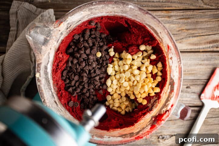 A generous amount of chocolate chips being folded into the rich, red velvet chocolate chip cookie dough.