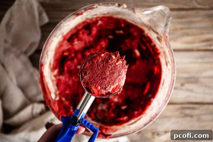 Using a trigger scoop to perfectly portion red velvet chocolate chip cookie dough onto a baking sheet, ensuring even size and baking.