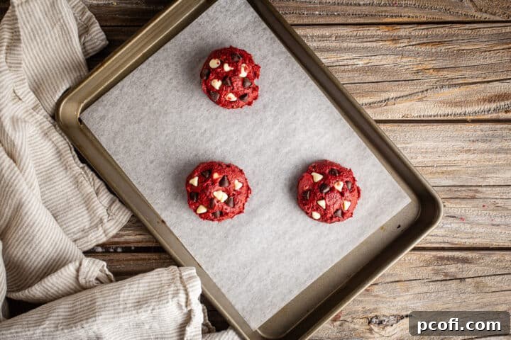 Unbaked red velvet chocolate chip cookies perfectly scooped onto a parchment-lined baking sheet, ready for the oven.