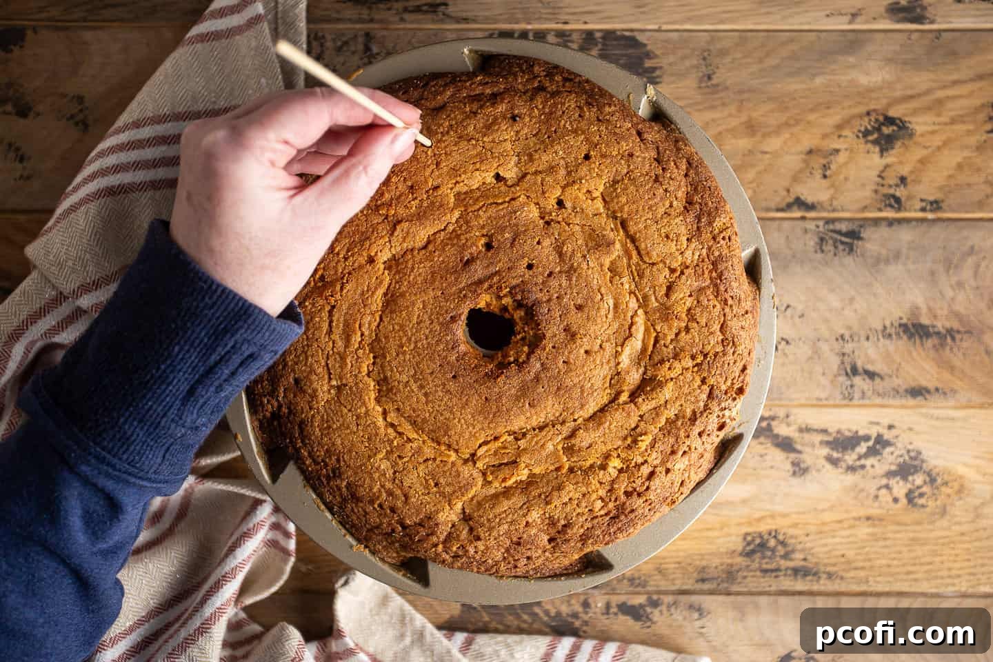 Poking holes into the bottom of a warm rum cake with a bamboo skewer, preparing it for the glaze.