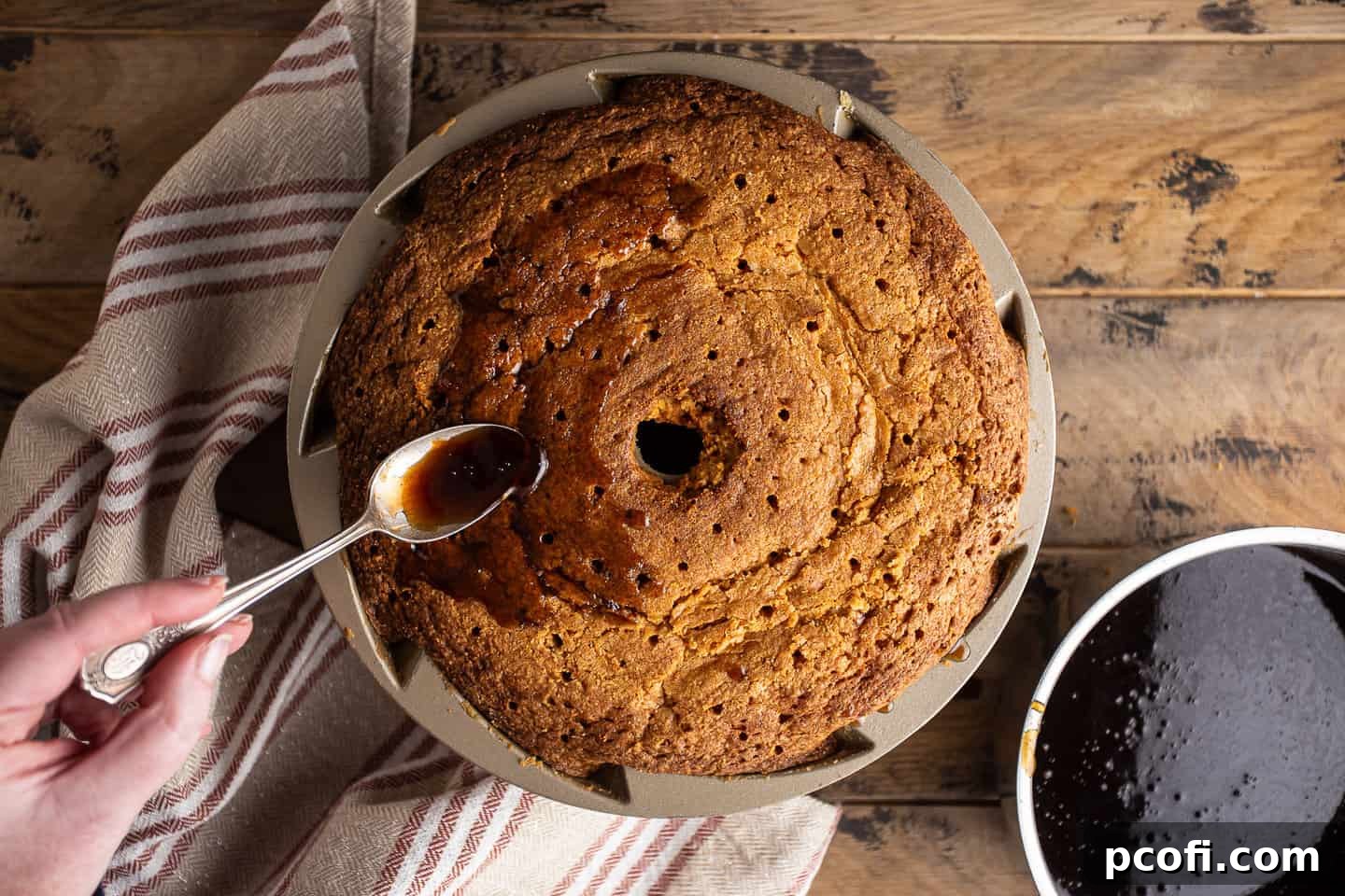 Spooning warm rum glaze over the surface of the rum cake, allowing it to soak in deeply.