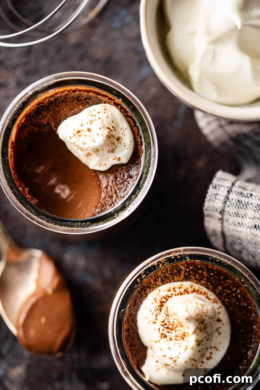 Three individual chocolate pots de creme, perfectly baked in small glass jars, beautifully topped with soft peaks of whipped cream, showcasing their smooth texture.