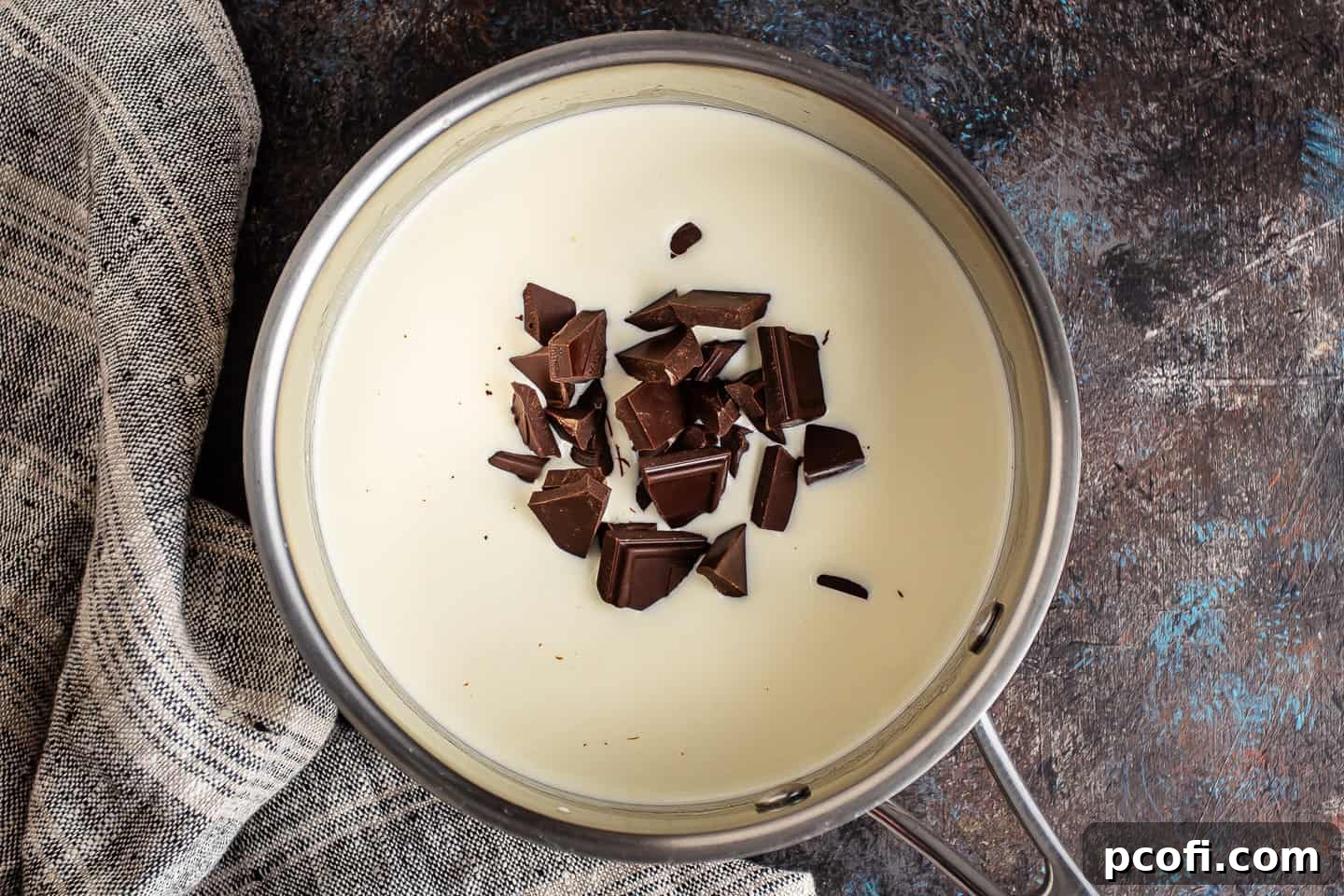 Heavy cream and broken chocolate pieces gently heating in a small stainless steel pot on the stovetop, starting the melting process.