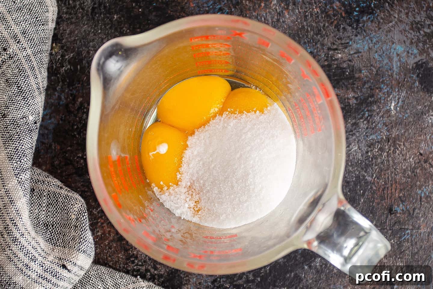 Egg yolks, granulated sugar, and kosher salt neatly arranged in a large glass measuring cup, ready for whisking.