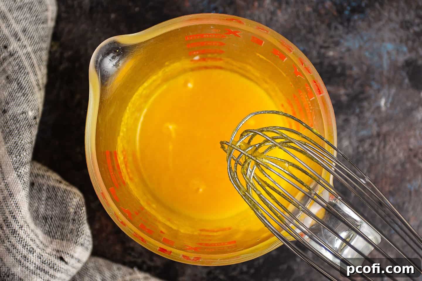 A whisk actively blending egg yolks, sugar, and salt together in a bowl until smooth and well-combined.