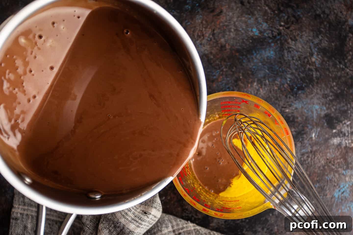 A steady stream of hot chocolate mixture being carefully poured into the egg yolks while continuously whisking to temper them properly.