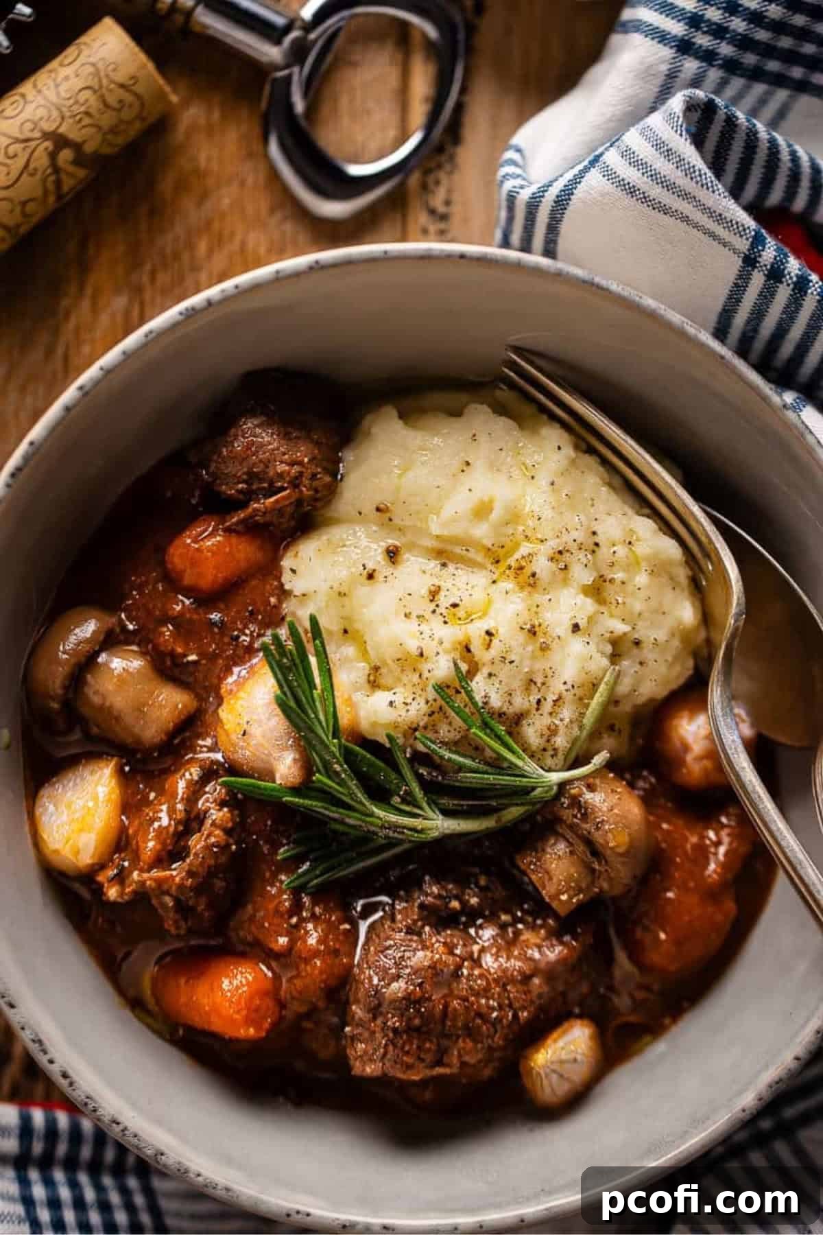 Classic Beef Bourguignon served in a rustic bowl with potatoes and a sprig of fresh rosemary.