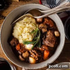 Beef Bourguignon in a bowl with mashed potatoes, garnished with rosemary.