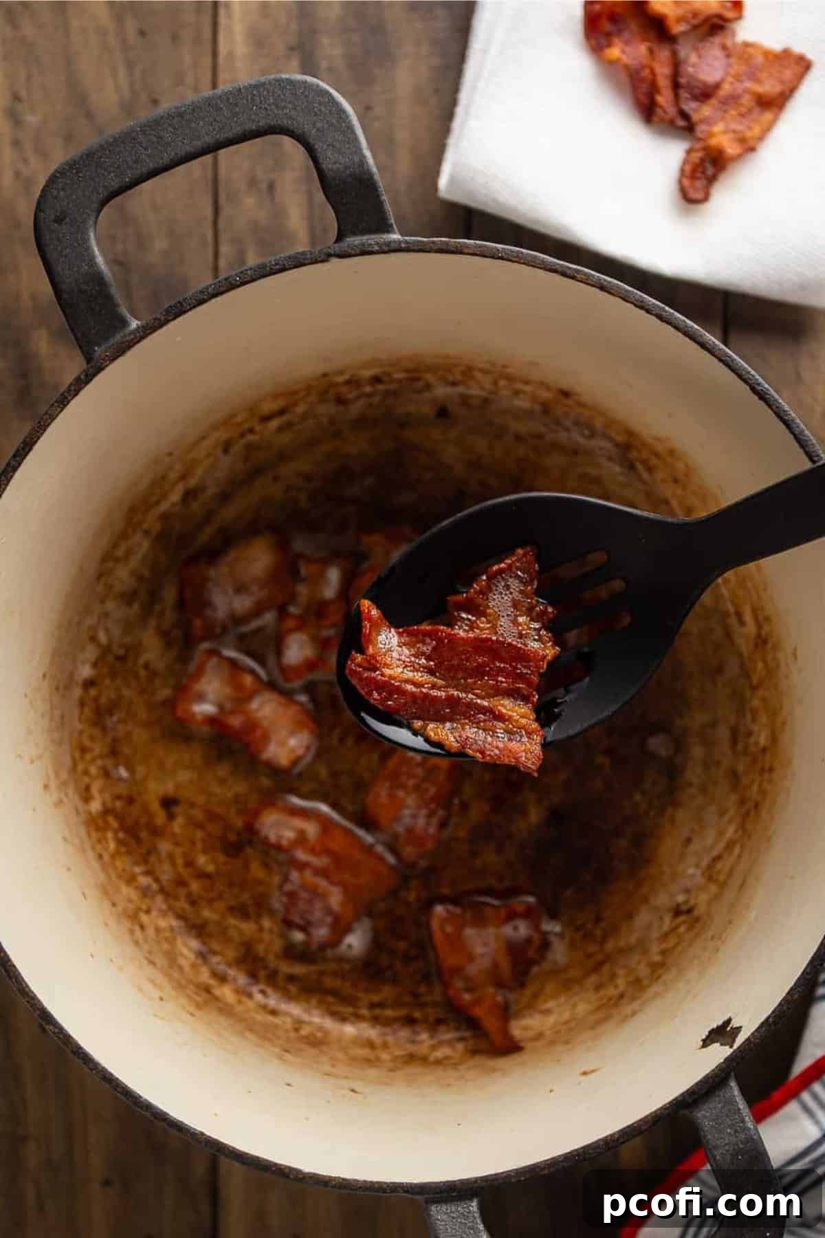 Cooked bacon pieces shown on a black spoon, removed from a pot.