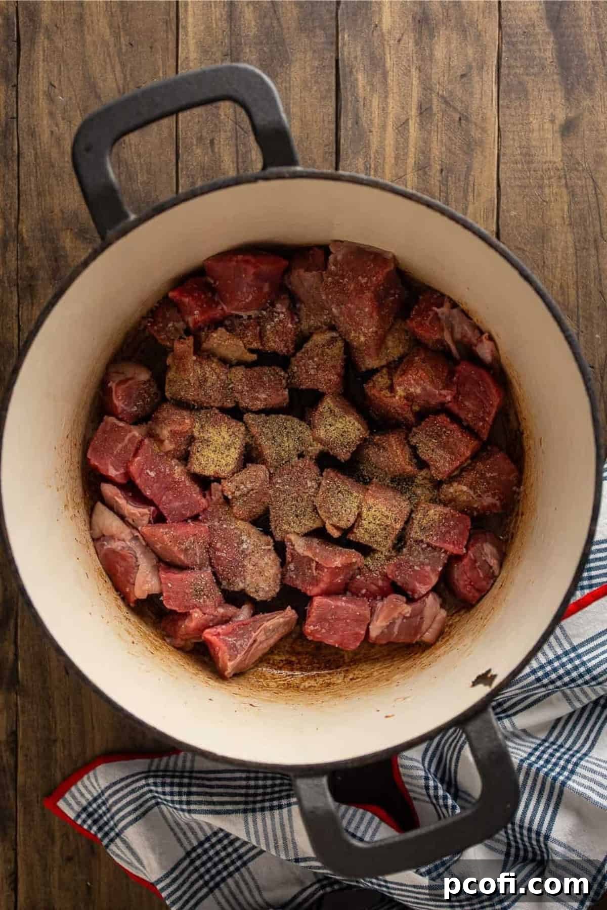 Beef chunks seasoned with spices being added to a pot for browning.