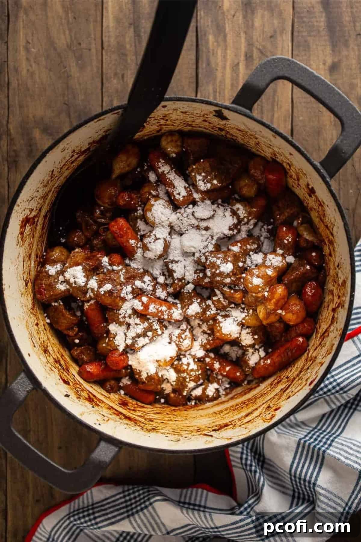 Flour sprinkled over cooked vegetables and beef chunks in a pot.