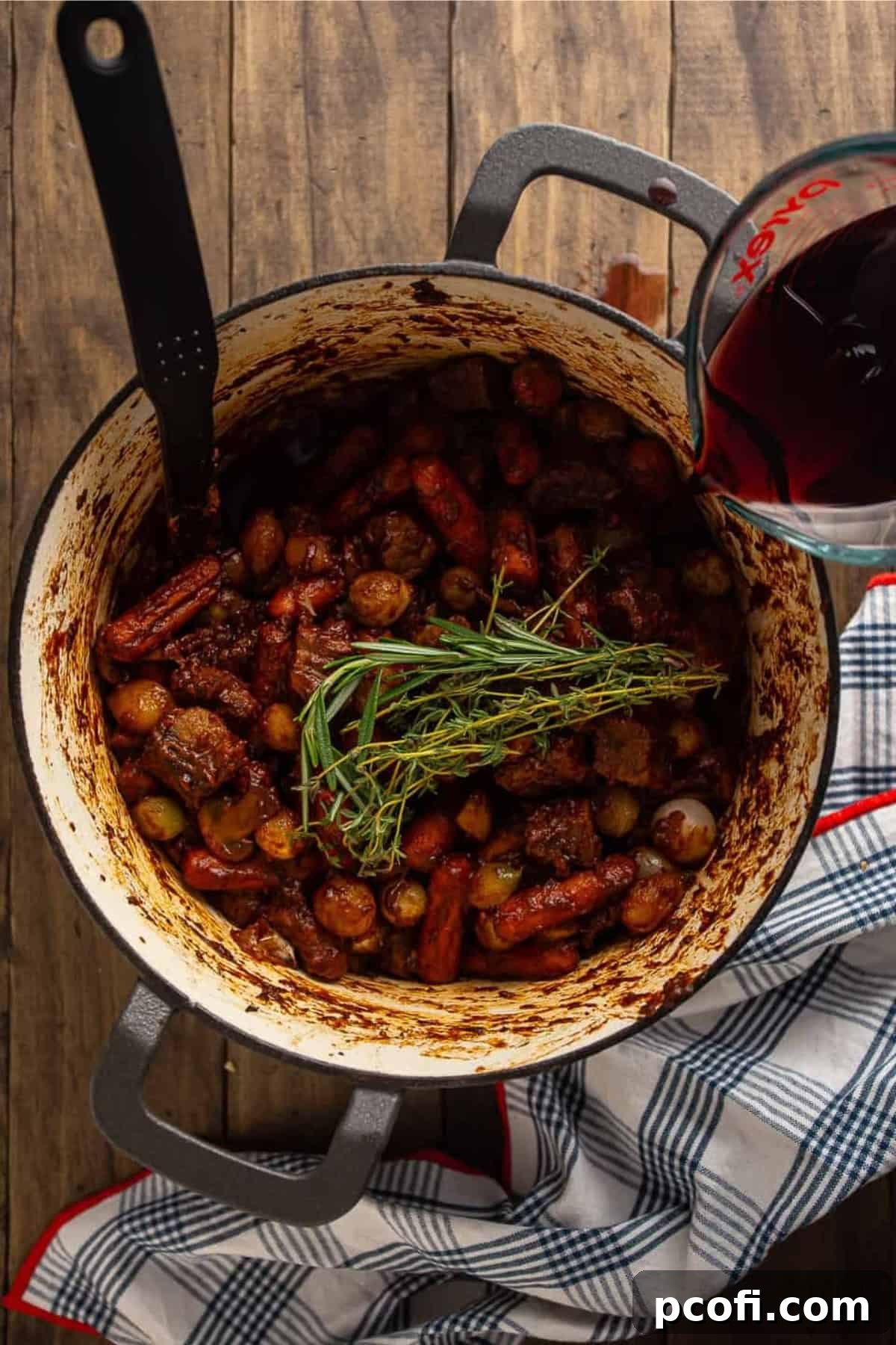 Beef, vegetables, and herbs simmering in a rich red wine sauce in a pot.