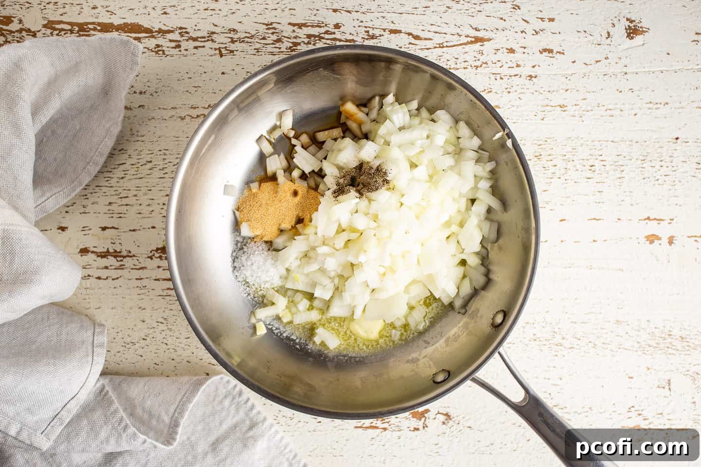 Chopped onions in a stainless steel skillet, with melted butter, Worcestershire sauce, salt, pepper, and garlic powder.