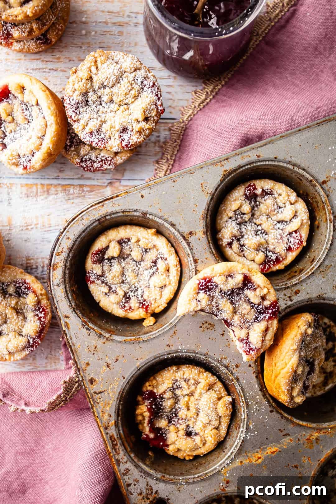 Baked mini raspberry jam tarts, still in the cupcake pan, golden and inviting.