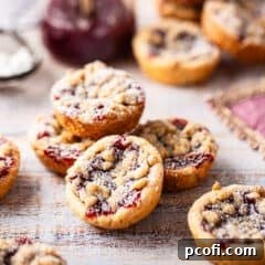 Mini raspberry tarts piled on a distressed wood surface.