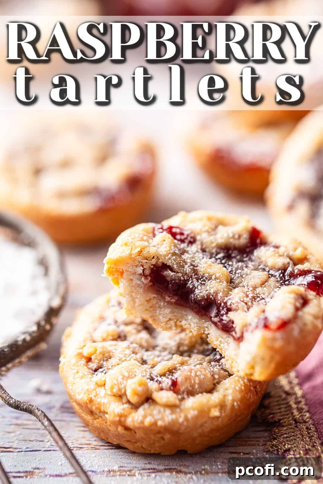 Close-up of a mini raspberry tart, revealing its jam filling and buttery streusel topping, ready to be enjoyed.