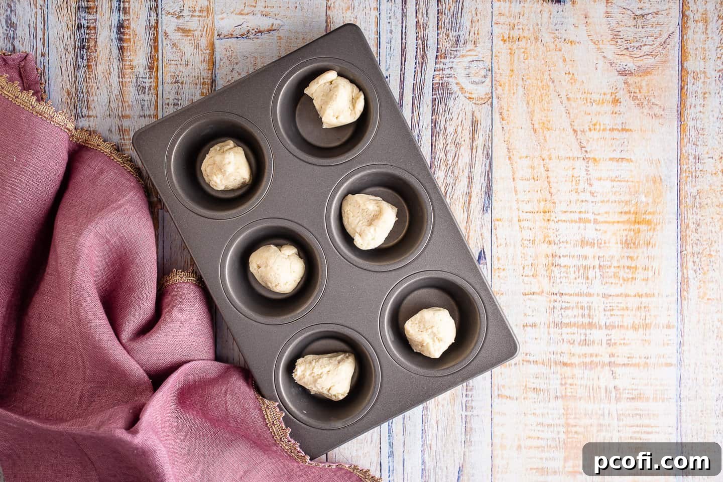 Placing small portions of tart dough into the wells of a cupcake pan, ready for shaping.
