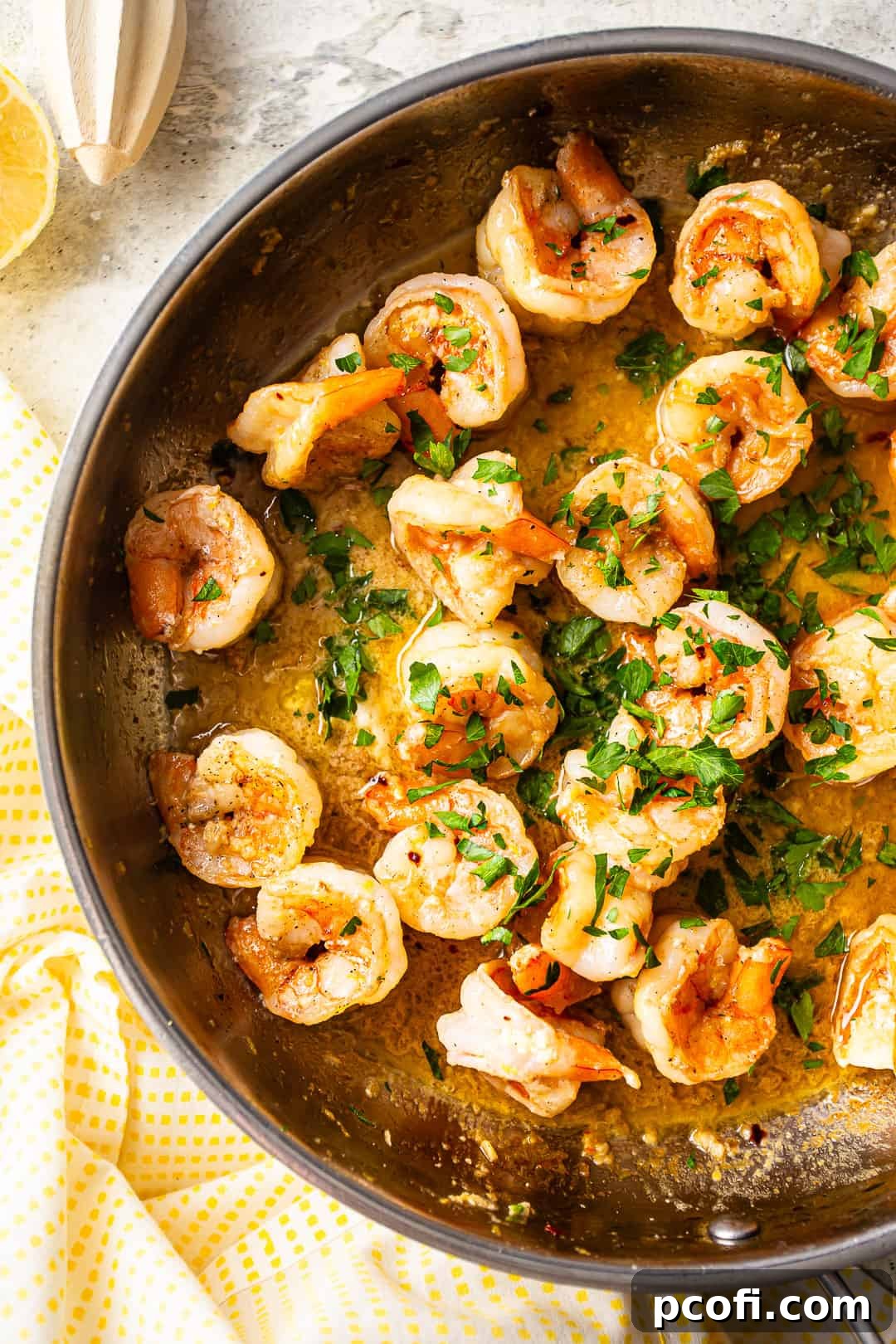 A close-up of thin spaghetti being tossed with shrimp scampi in a large skillet, coated in a glistening garlic and lemon sauce.