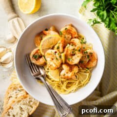 Shrimp scampi served over pasta in a white ceramic bowl.