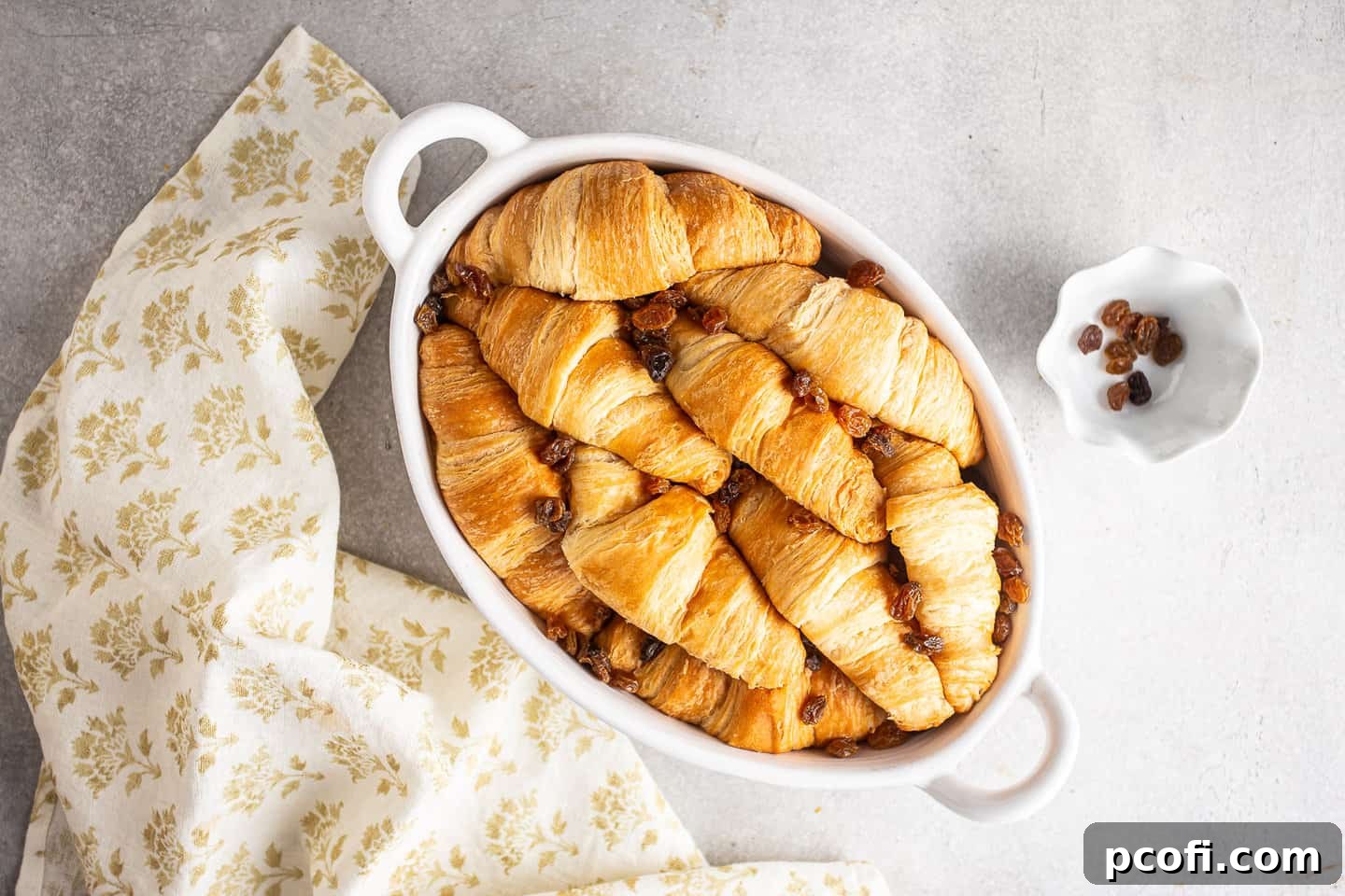Croissants and golden raisins arranged in a baking dish.