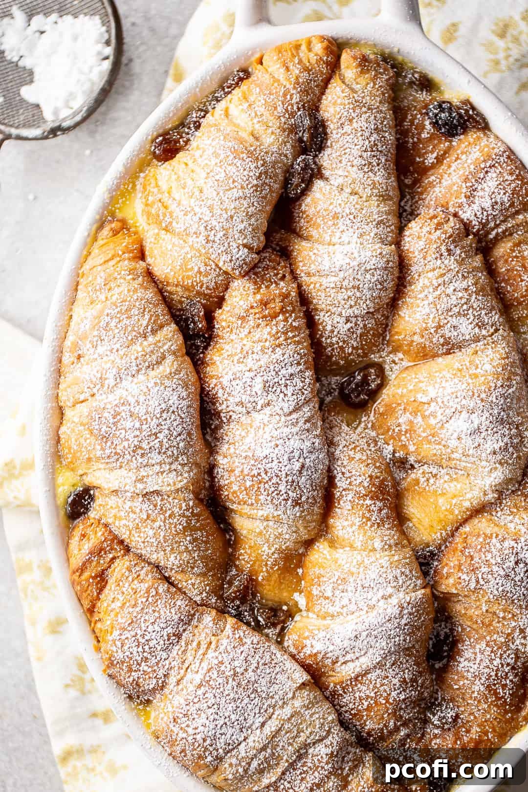 Bread pudding with croissants recipe, speckled with golden raisins and dusted with powdered sugar.
