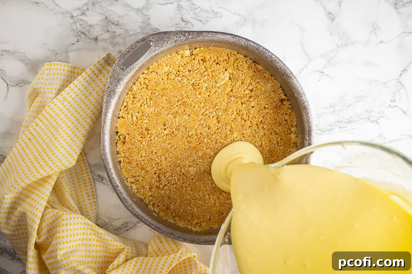 Pouring the smooth lemon cheesecake batter over the already prepared shortbread cookie crust in the cake pan.