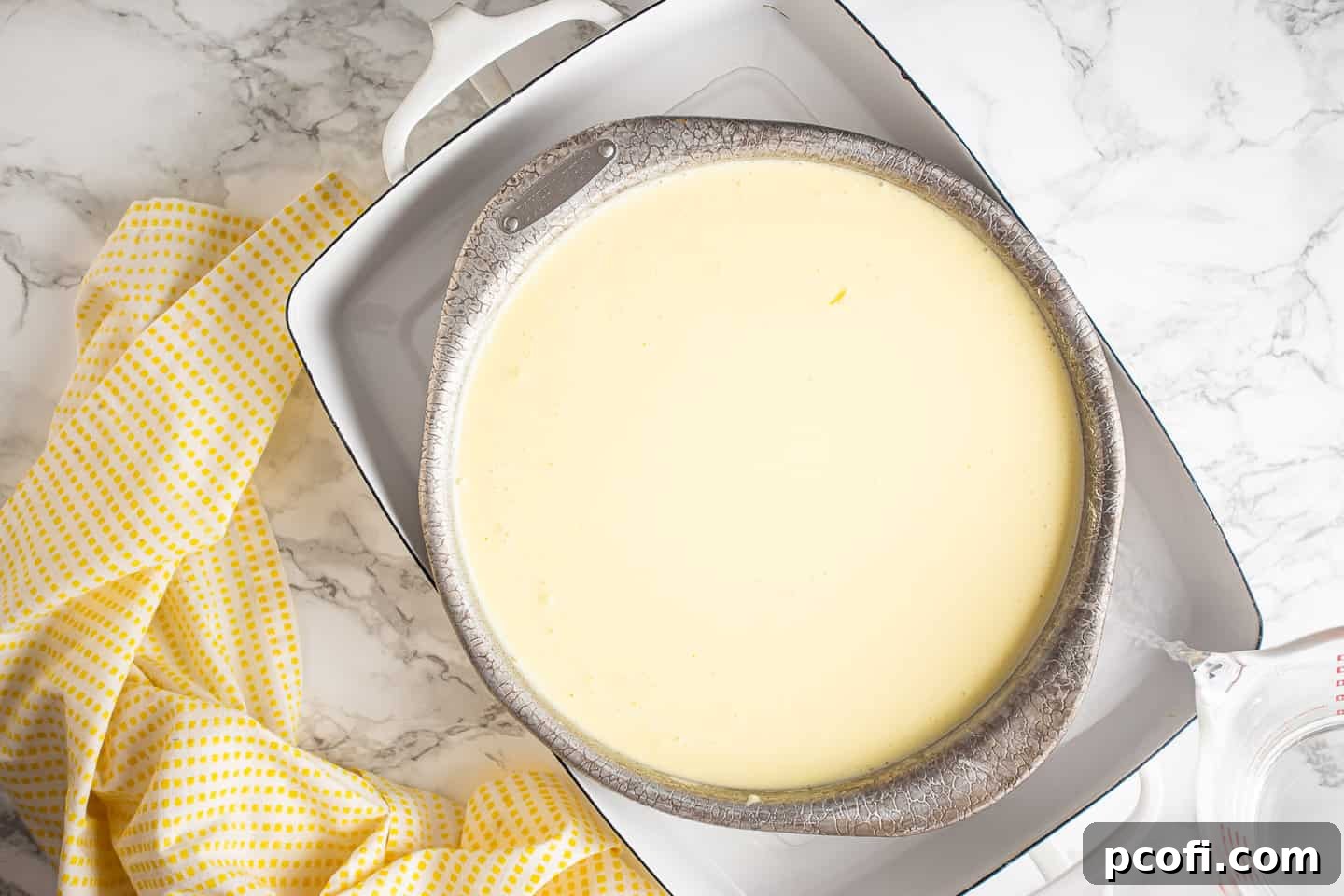 Unbaked lemon cheesecake placed in a larger pan filled with water, ready for baking in a water bath to ensure even cooking.