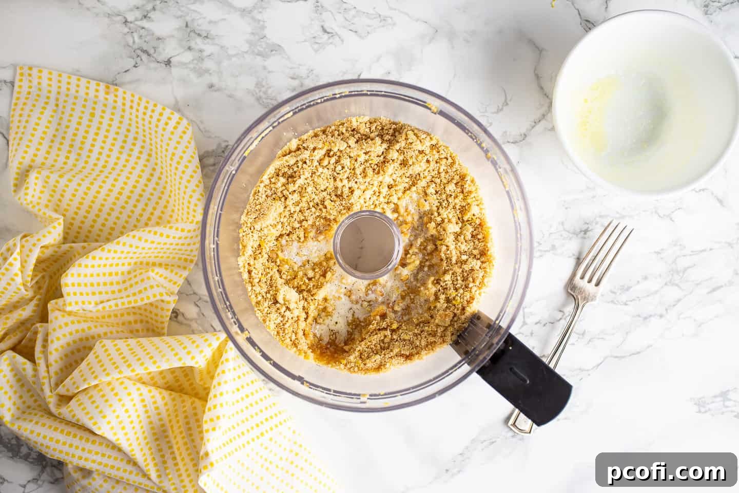 Adding melted butter to the crushed shortbread cookies and lemon zest mixture, preparing it for the cheesecake crust.