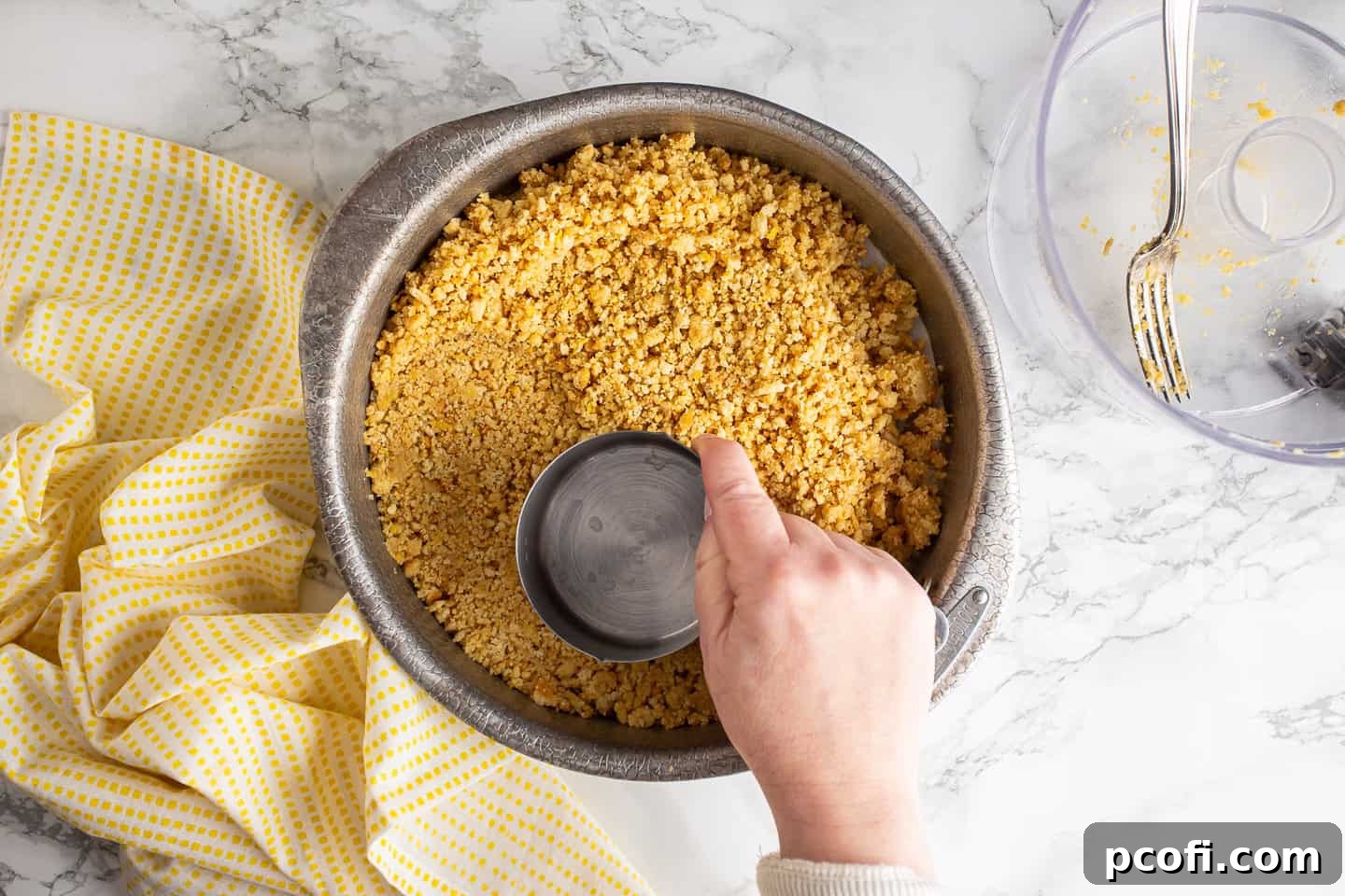 Pressing the lemon shortbread crust mixture firmly into the bottom of a cake pan using a measuring cup to ensure an even layer.
