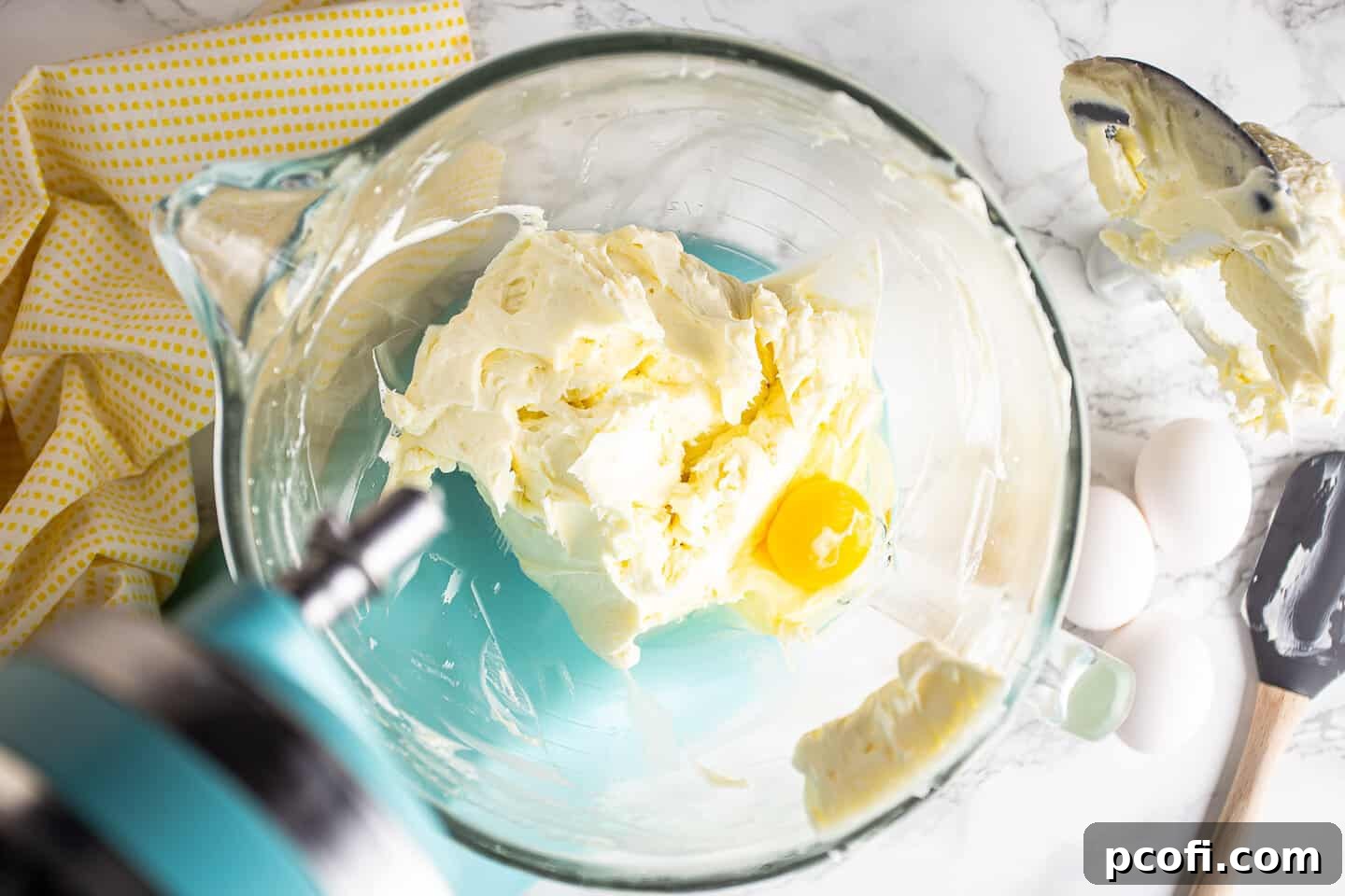 Adding eggs one by one to the lemon cheesecake batter, ensuring each is fully incorporated before adding the next for a smooth consistency.