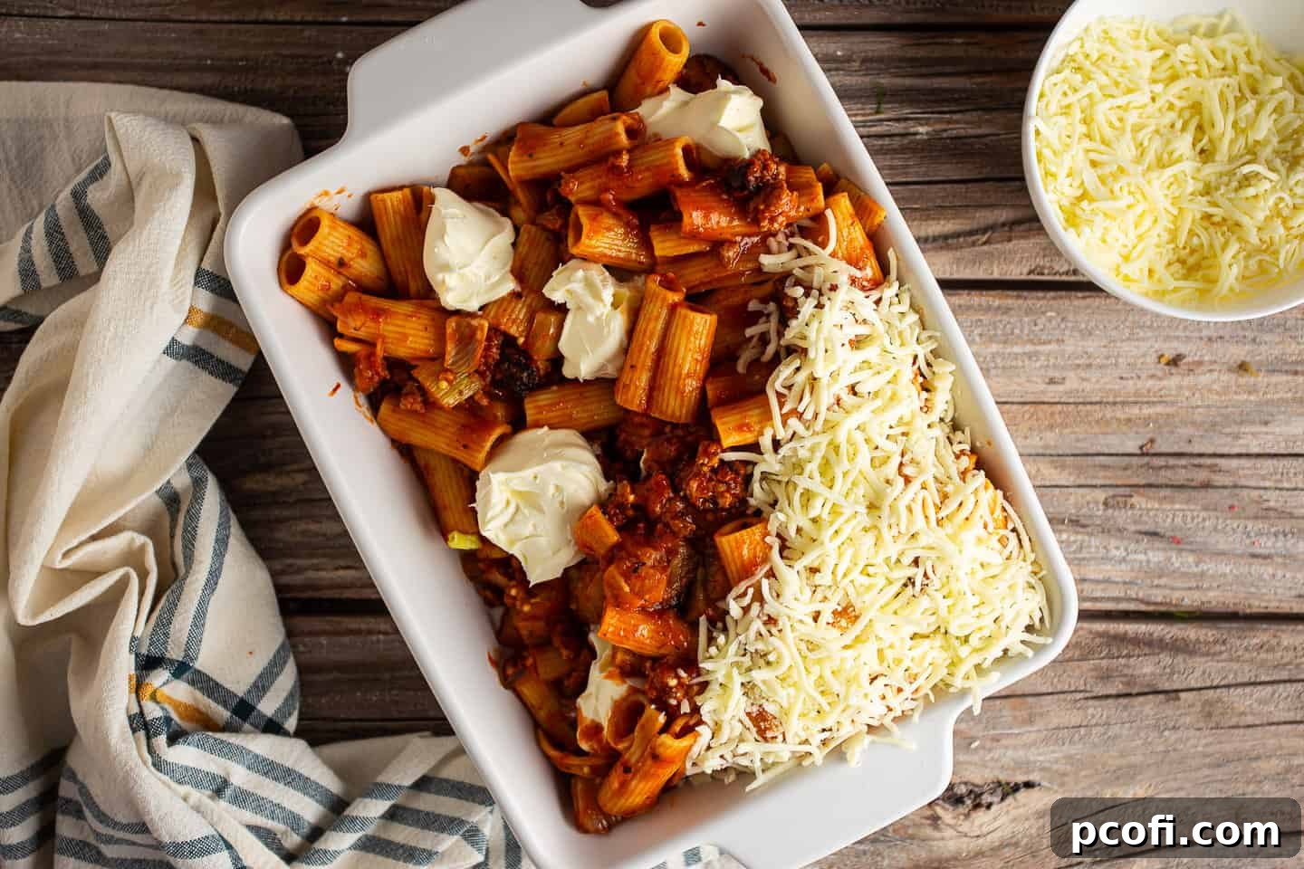 The final step of layering shredded mozzarella cheese over a pan of sausage rigatoni before baking.