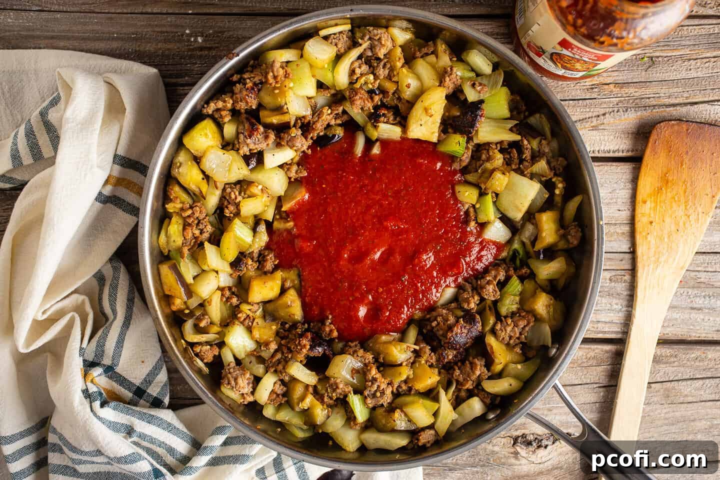 Adding rich tomato sauce to the mixture of cooked sausage, fennel, and eggplant.