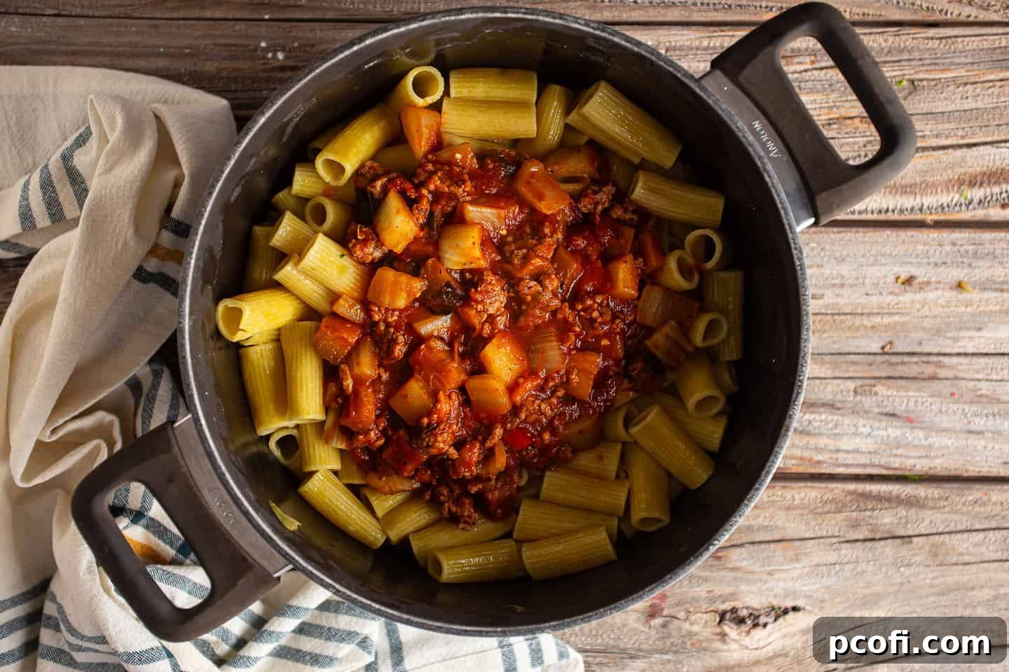 Tossing cooked rigatoni pasta with a rich sauce, sausage, and vegetables in a large pot.
