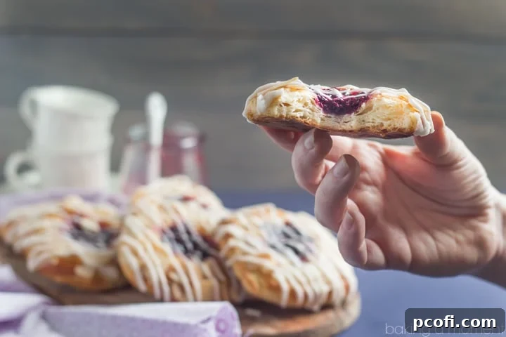 A top-down view of several Blackberry Ginger Danish pastries, showcasing their golden crust, the vibrant filling peek, and the sweet vanilla glaze drizzle.