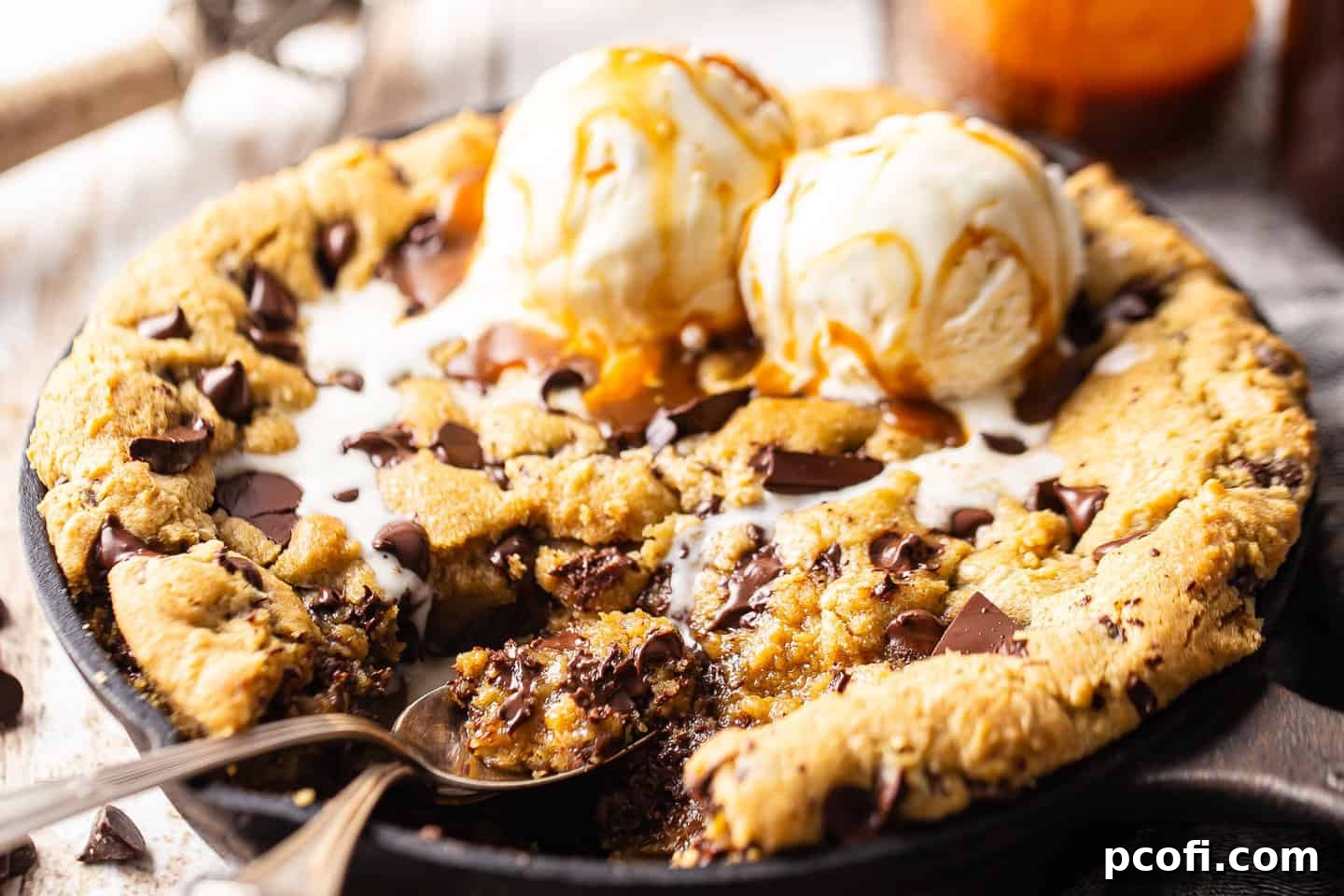 Cast iron skillet cookie with chocolate chips, a scoop of vanilla ice cream, and a drizzle of caramel sauce, ready to be served.