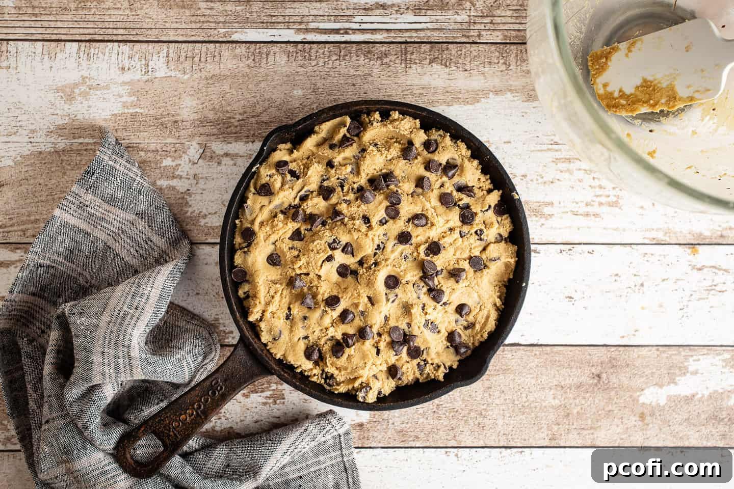 Chocolate chip cookie dough pressed into an 8-inch cast iron skillet, ready for baking.