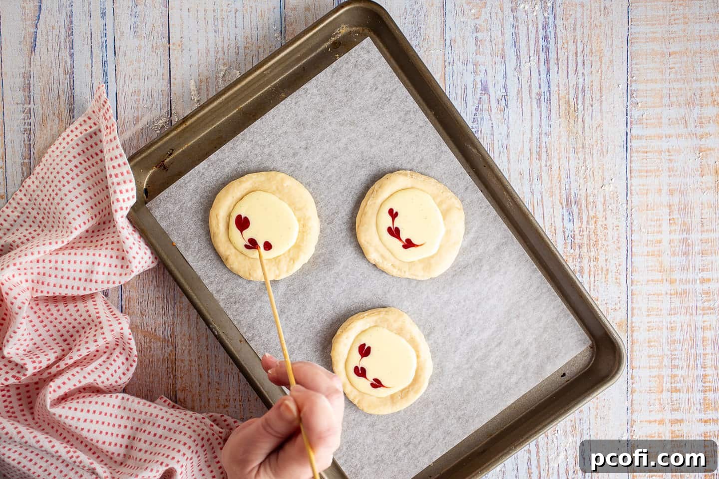 Unbaked Cheese Danish pastries being garnished with raspberry sauce hearts on the cream cheese filling.