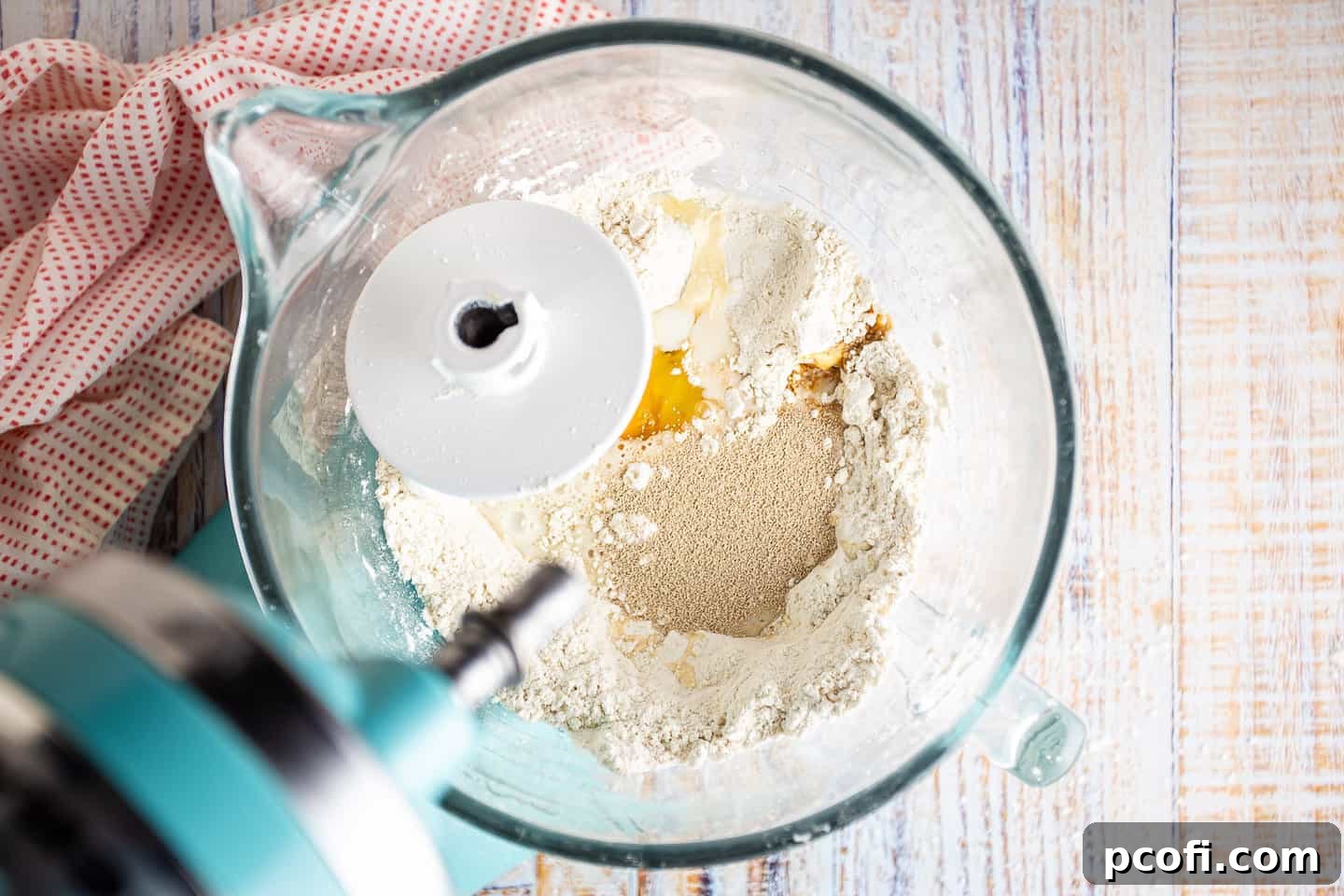 Liquid ingredients and yeast added to the dry ingredients in a mixing bowl for Danish dough.