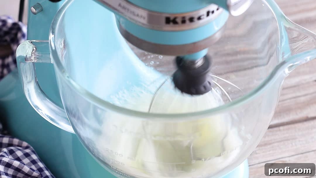Egg whites and cream of tartar being whipped in a mixer, reaching the soft peak stage crucial for a stable meringue.