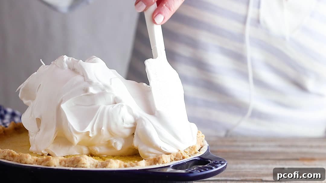 Fluffy white meringue being carefully spread over the warm lemon pie filling, extending to the crust's edge to prevent shrinkage.