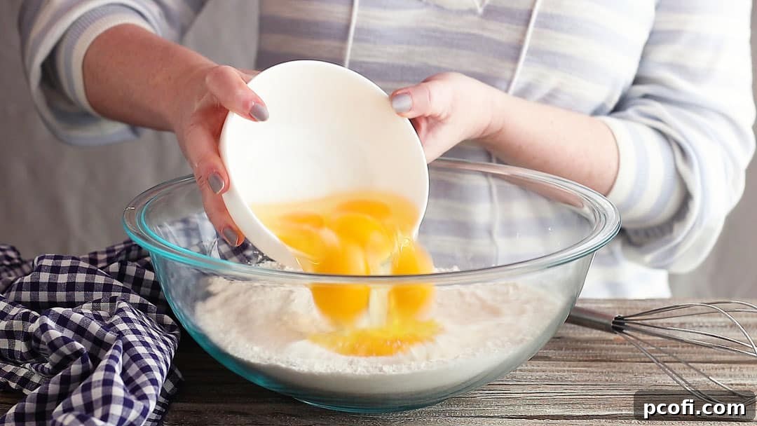Adding a generous quantity of eggs to the dry ingredients for the lemon meringue pie filling in a large glass bowl, ensuring a rich and firm custard.